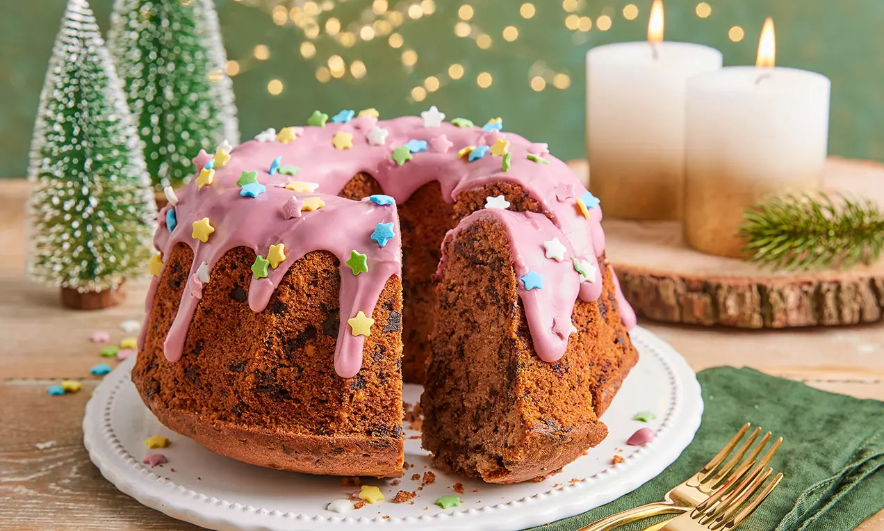 Rózsaszín mázzal csorgatott vörösboros kuglóf csillag alakú színes szórócukorral, szeletelve fehér tányéron, gyertyák és fenyődíszek között
